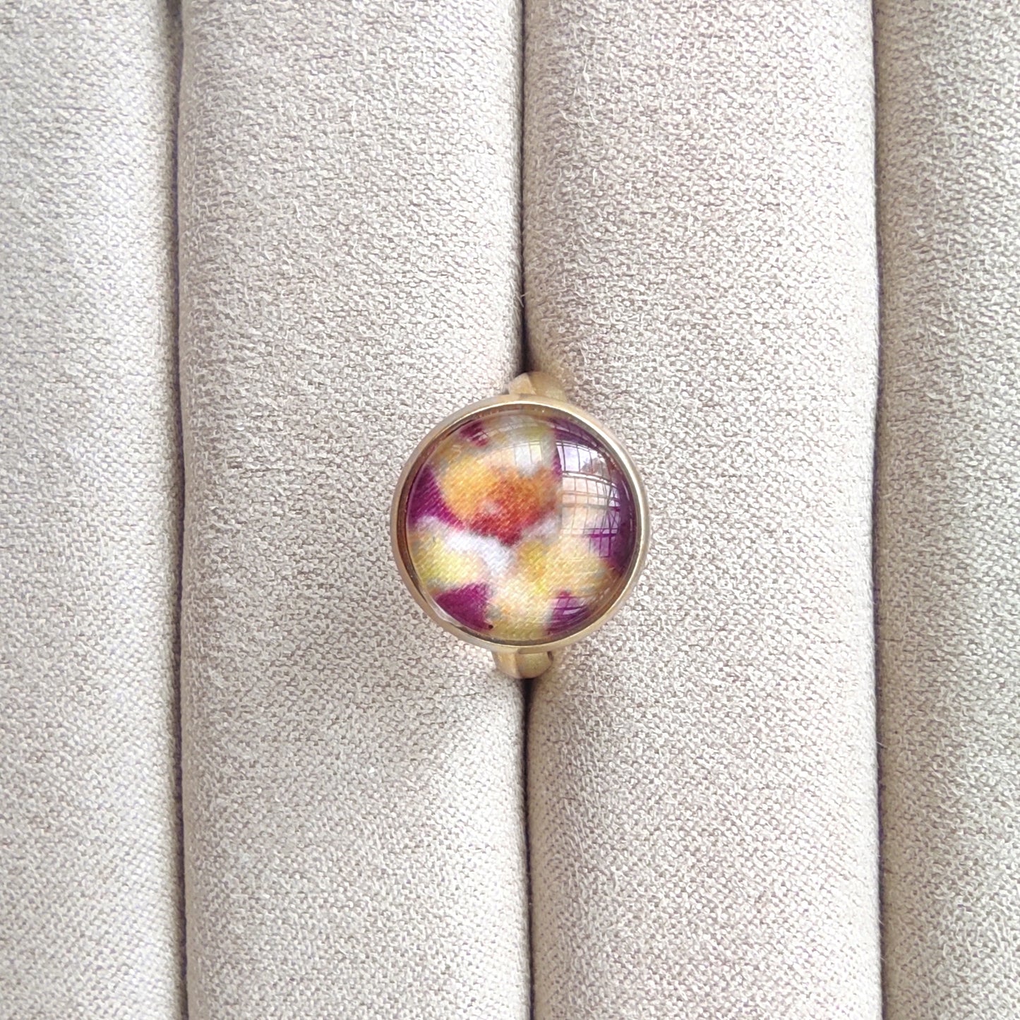 Bague acier inoxydable réglable motif floral, motif fleurs dorées avec fond violet. Une fleur jaune est placée au centre de la bague doré.