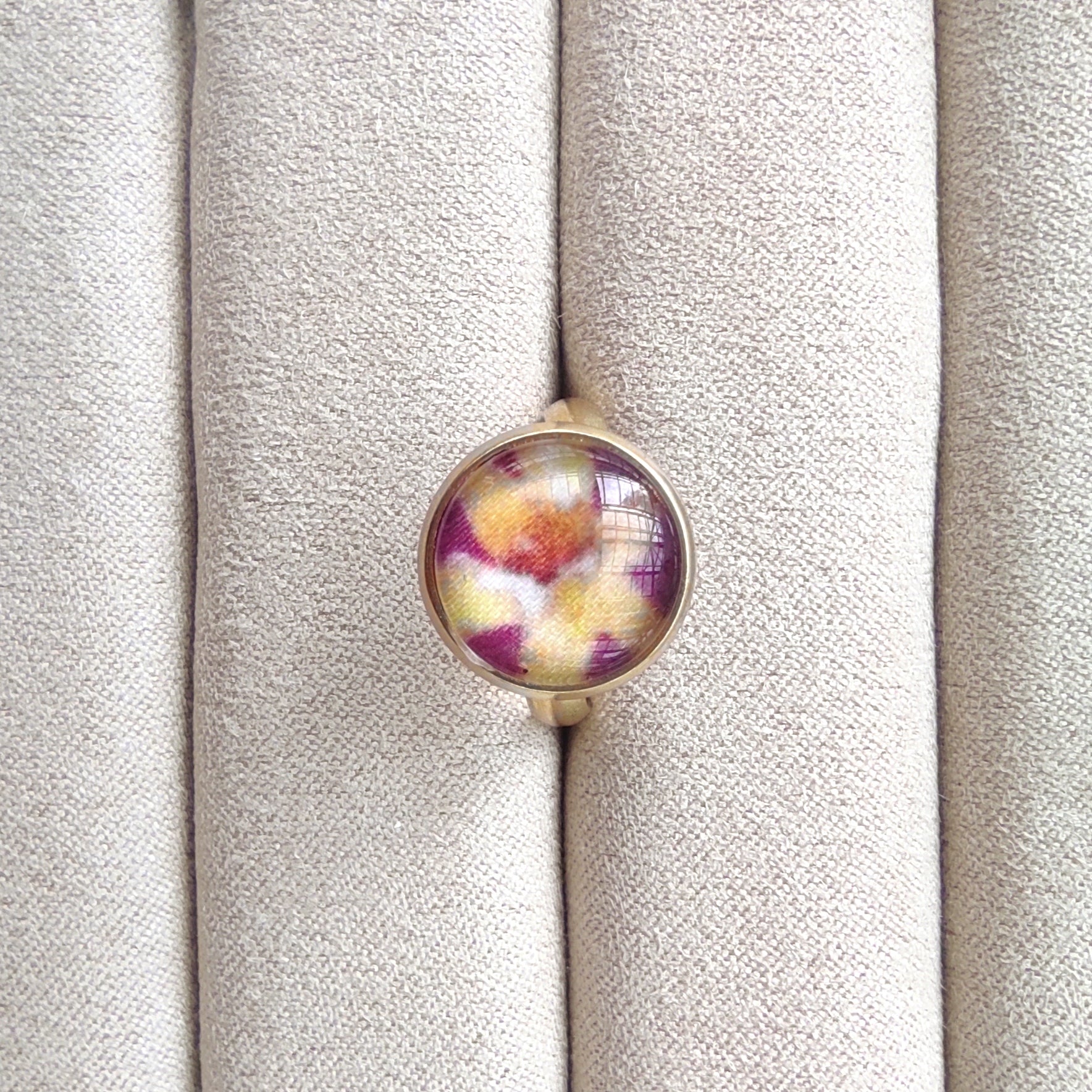 Bague acier inoxydable réglable motif floral, motif fleurs dorées avec fond violet. Une fleur jaune est placée au centre de la bague doré.
