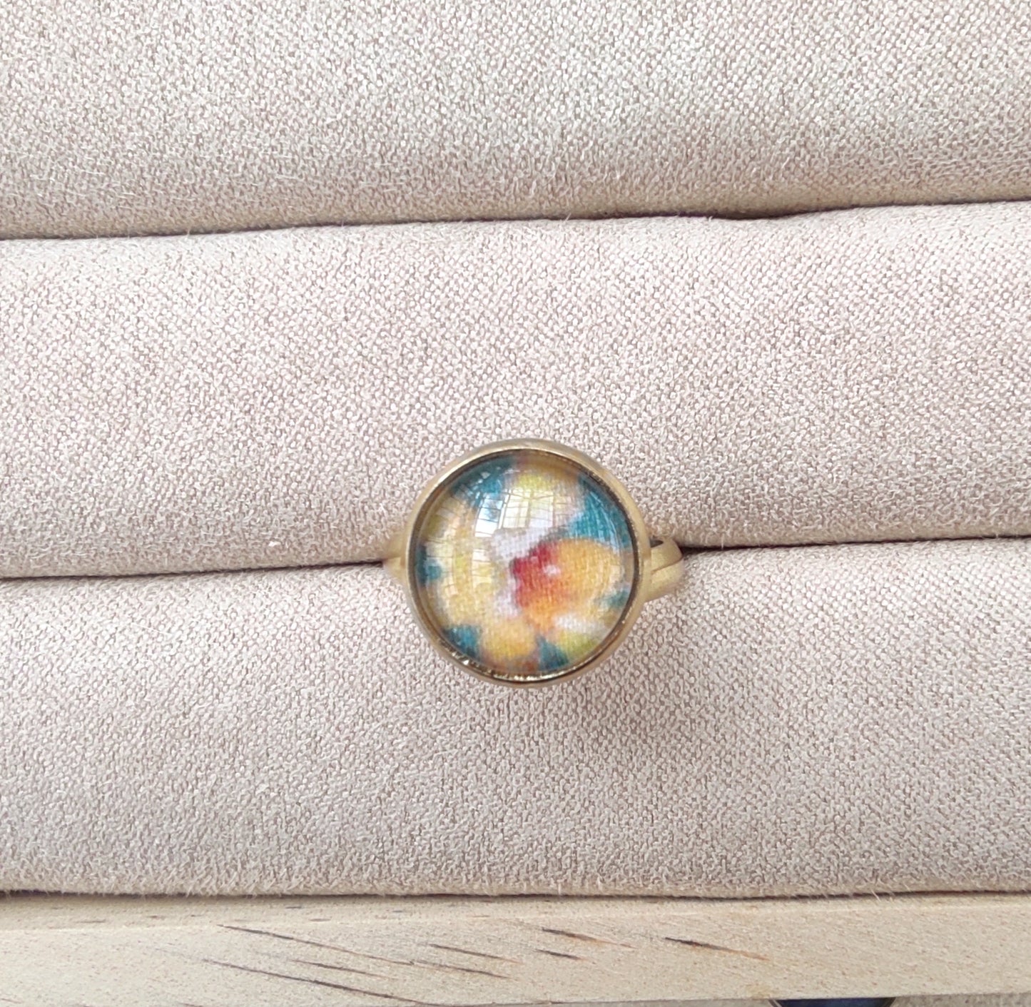 Bague acier inoxydable réglable motif floral, motif fleurs dorées avec fond vert. Une fleur jaune est placée au centre de la bague doré.