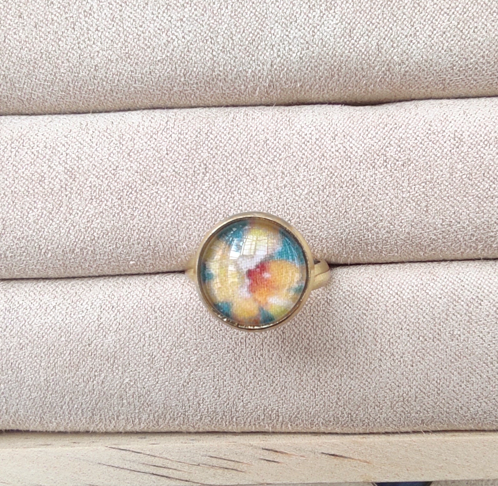 Bague acier inoxydable réglable motif floral, motif fleurs dorées avec fond vert. Une fleur jaune est placée au centre de la bague doré.