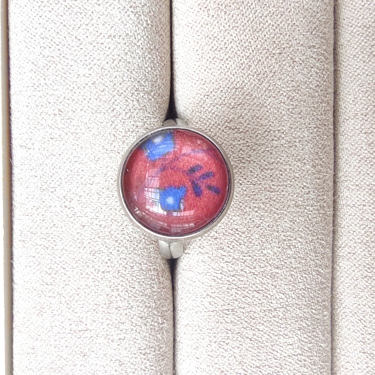 Bague acier inoxydable réglable motif floral, motif fleurs bleues fond paprika. Des fleurs bleues avec feuillage sont placés au centre avec un fond couleur paprika.