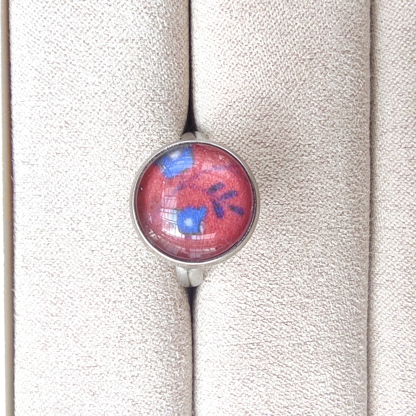 Bague acier inoxydable réglable motif floral, motif fleurs bleues fond paprika. Des fleurs bleues avec feuillage sont placés au centre avec un fond couleur paprika.