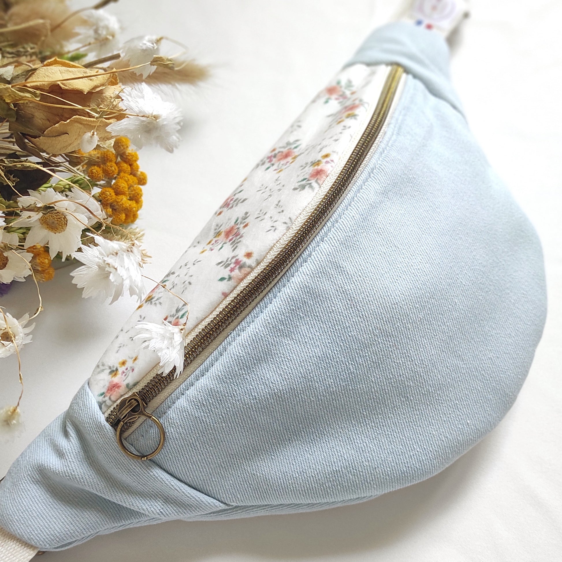 Banane conçue par Fanny Agustin- fabrication artisanale française- Banane vue de face, avec jean bleu clair et dessus de la banane avec tissu en velours fleuri blanc et quelques touches de couleur saumoné, jaune et vert.