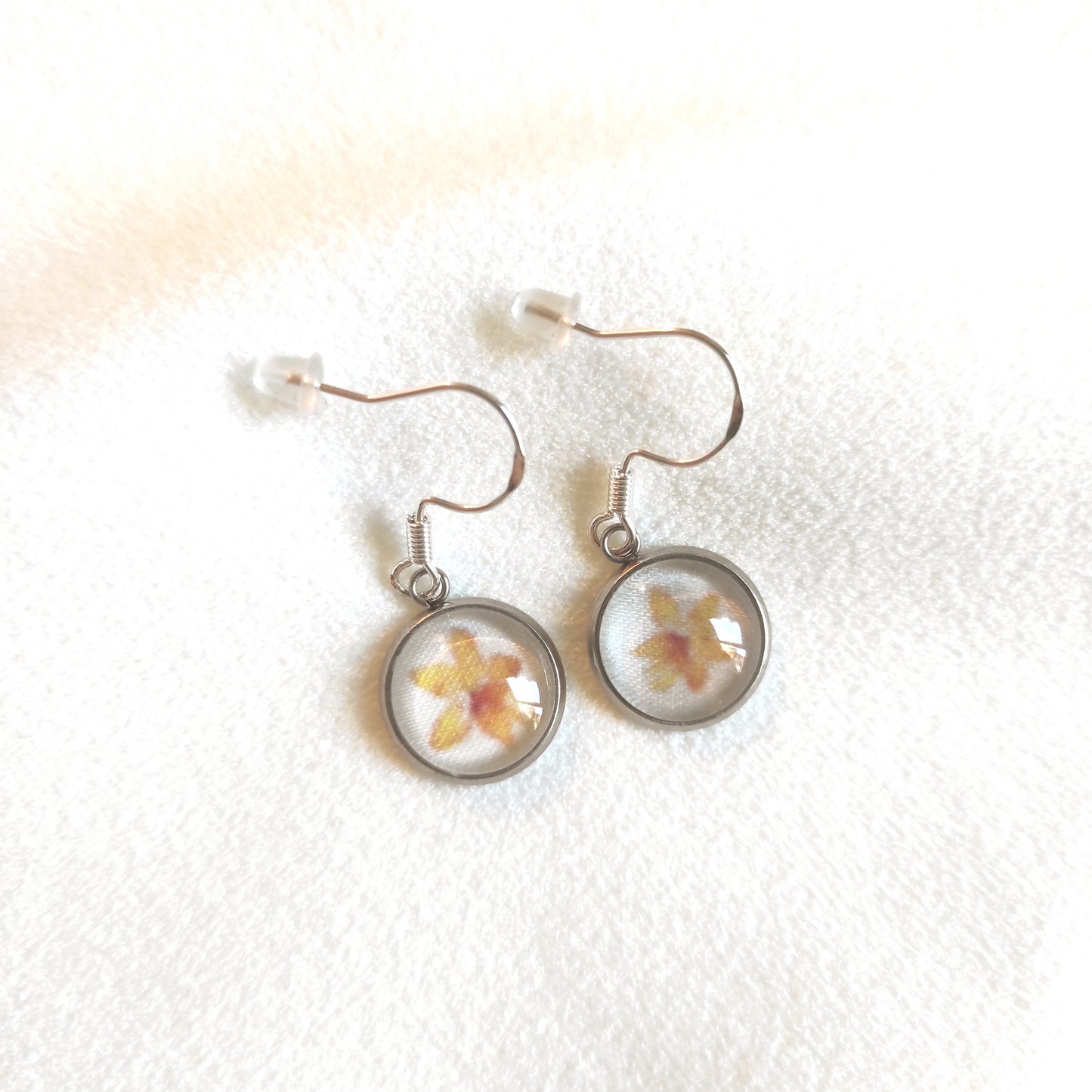 Boucles d'oreille en acier inoxydable motif fleuri avec fleurs jaunes au centre et fond blanc. Taille du pendentif 12 mm de diamètre.