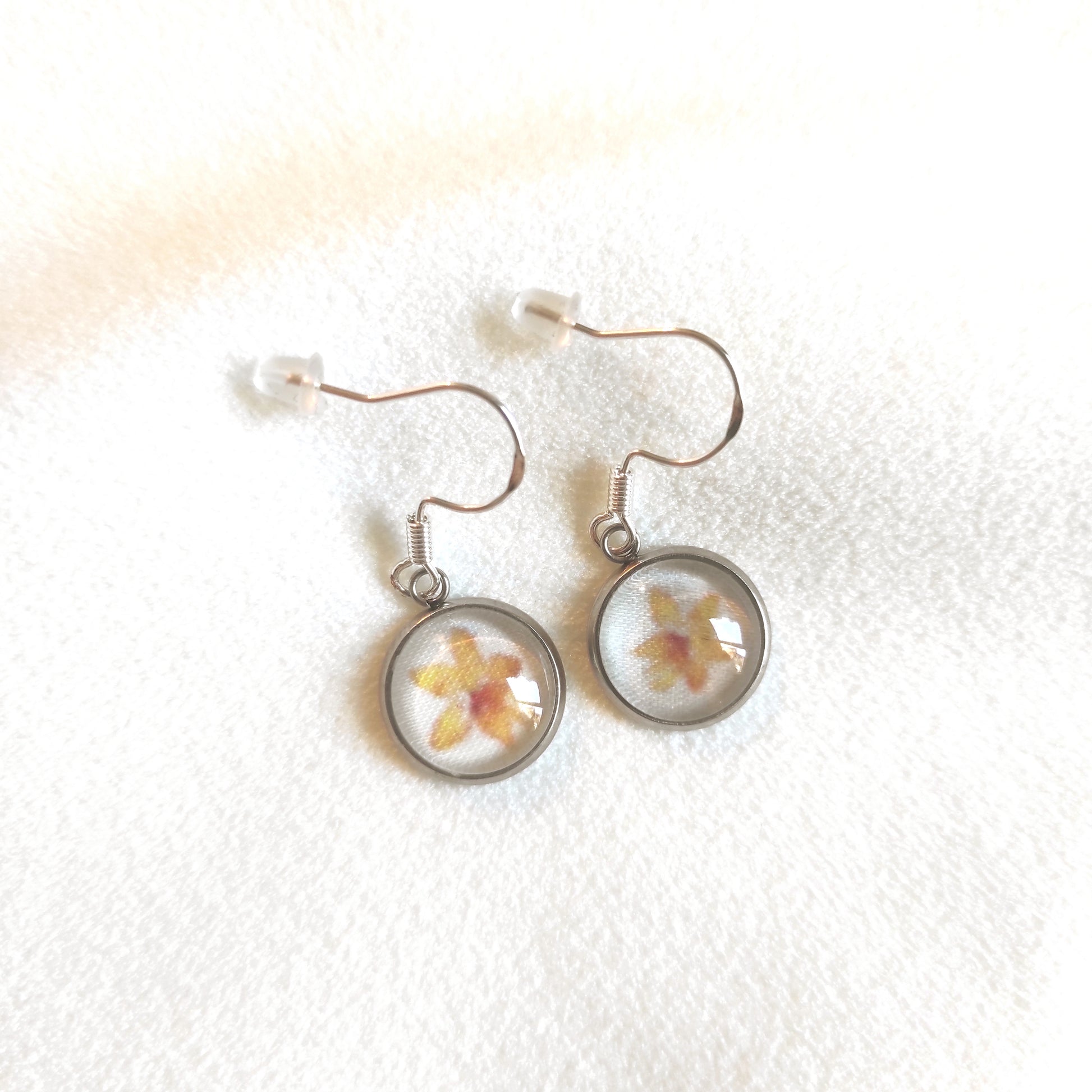 Boucles d'oreille en acier inoxydable motif fleuri avec fleurs jaunes au centre et fond blanc. Taille du pendentif 12 mm de diamètre.
