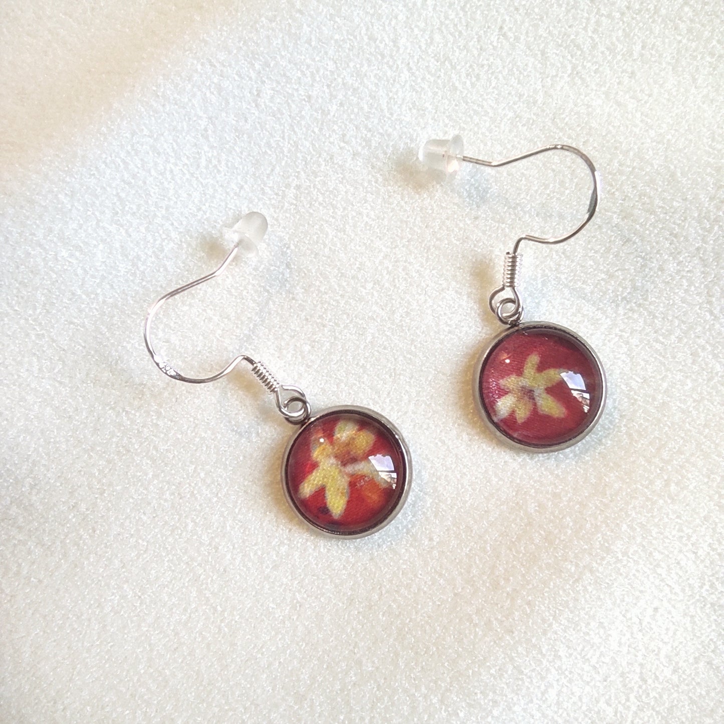 Boucles d'oreille en acier inoxydable motif fleuri rouge. La couleur de l'acier est couleur argent, avec motif fleurs jaunes et fond rouge.