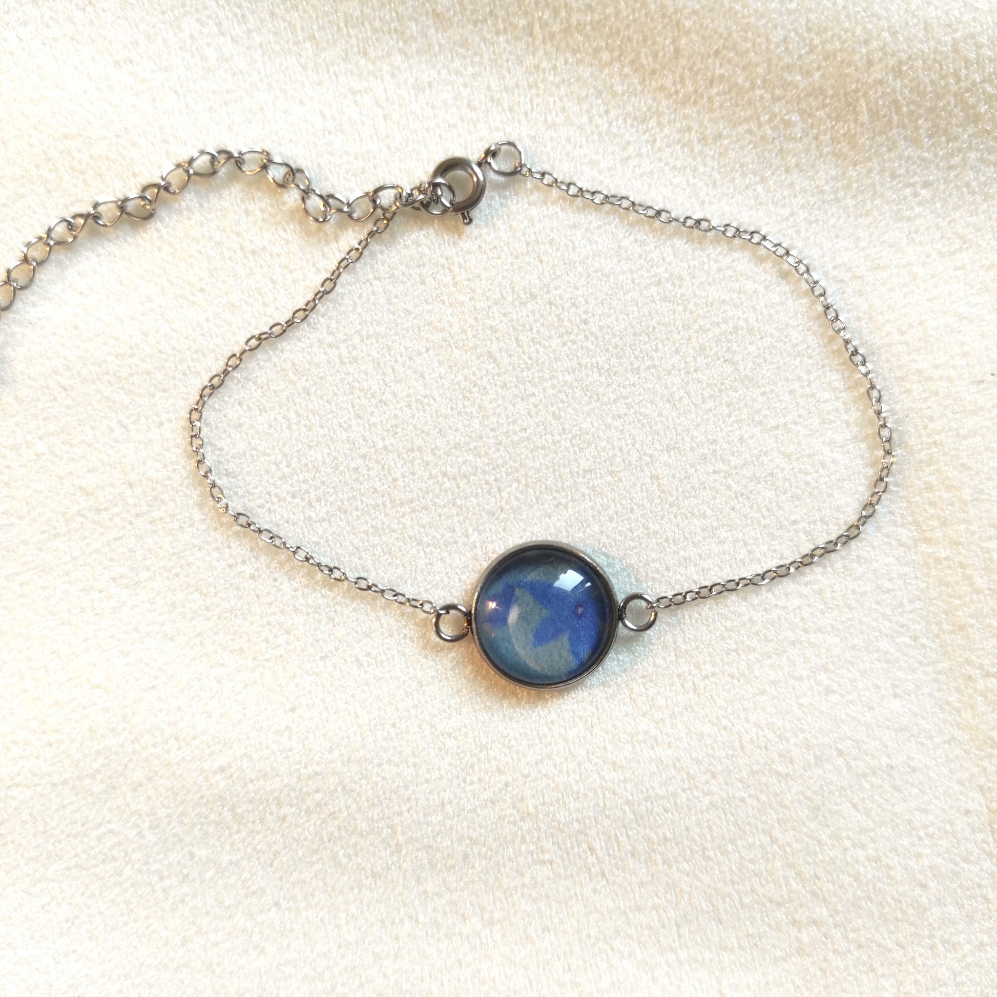 Bracelet réglable acier inoxydable couleur argenté positionné sur un présentoir. Le motif à l'intérieur comporte des fleurs bleues avec un fond bleu. Perle de 12 mm de diamètre. Bracelet fait main par Fanny Agustin.