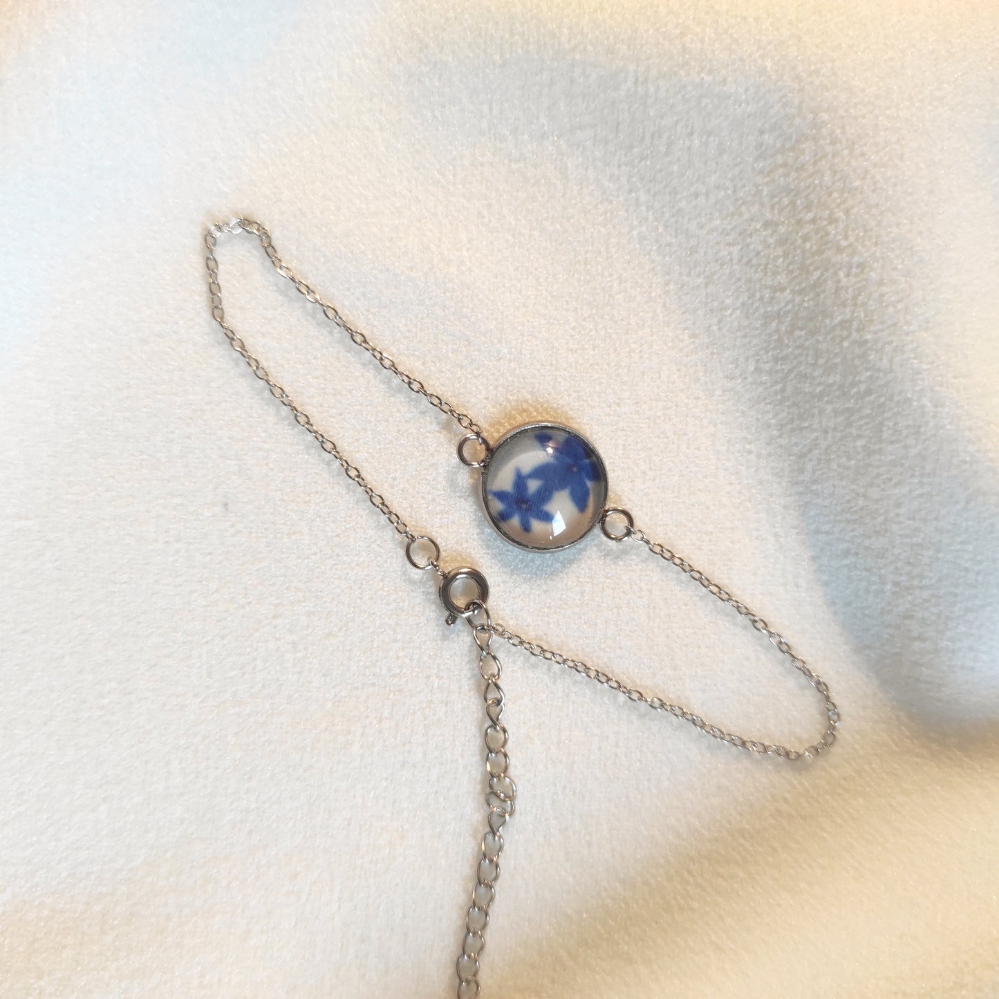 Bracelet réglable acier inoxydable couleur argenté positionné sur un tissu blanc. Le motif à l'intérieur comporte des fleurs bleues avec un fond blanc. Perle de 12 mm de diamètre.