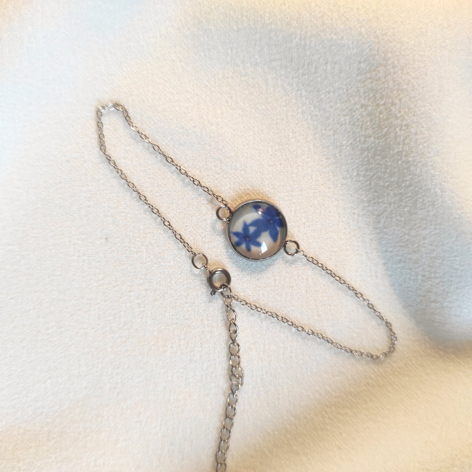 Bracelet réglable acier inoxydable couleur argenté positionné sur un tissu blanc. Le motif à l'intérieur comporte des fleurs bleues avec un fond blanc. Perle de 12 mm de diamètre.