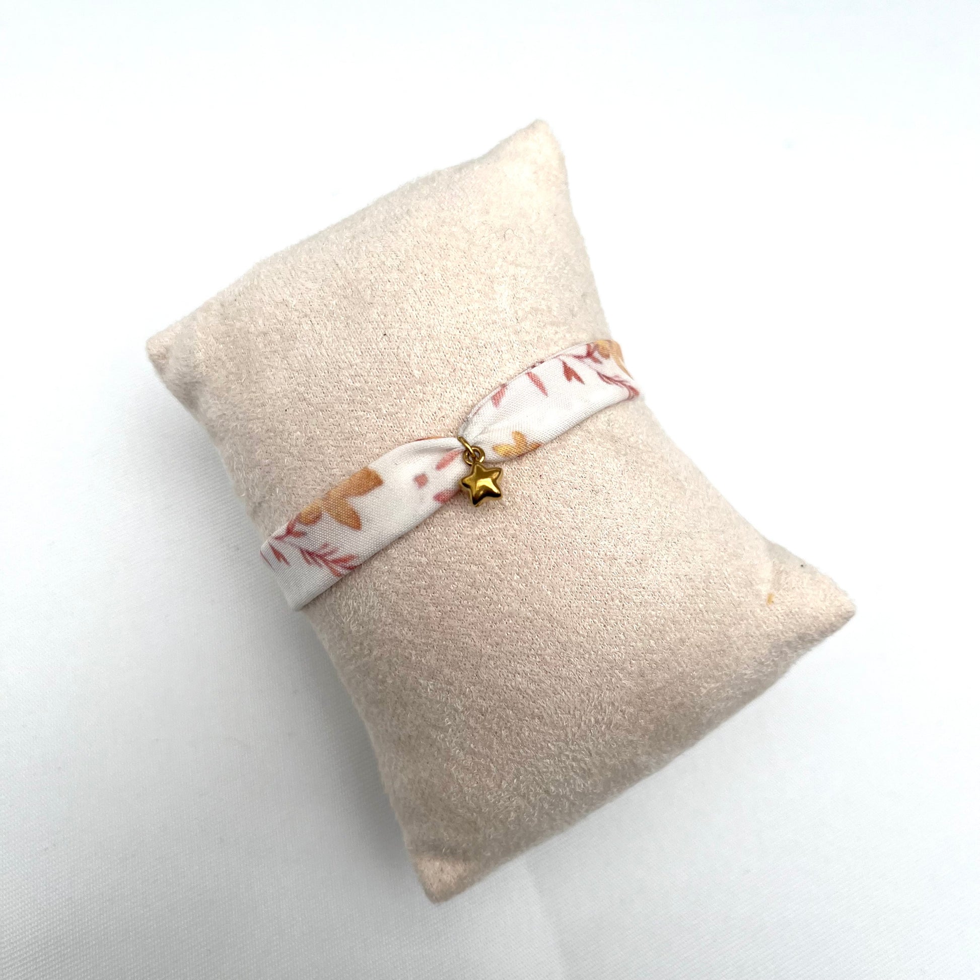 Bracelet en tissu signé Fanny Agustin, le motif est blanc, marron et jaune, il représente des fleurs avec feuillage. La breloque est une étoile dorée. 
