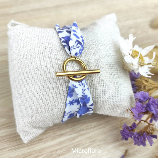 Bracelet en tissu fleuri dessiné par Fanny Agustin. Le motif est bleu et blanc, imprimé localement sur du tissu en microfibre avec fermoir en T couleur doré.