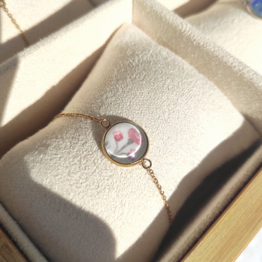 Bracelet réglable acier inoxydable couleur doré positionné sur un présentoir. Le motif à l'intérieur est une fleur rose avec un fond blanc. Perle de 12 mm de diamètre.