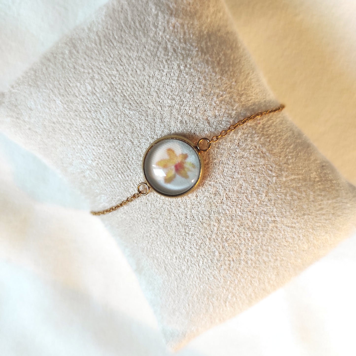 Bracelet réglable acier inoxydable couleur doré positionné sur un présentoir. Le motif à l'intérieur comporte une fleur jaune avec un fond blanc. Perle de 12 mm de diamètre.
