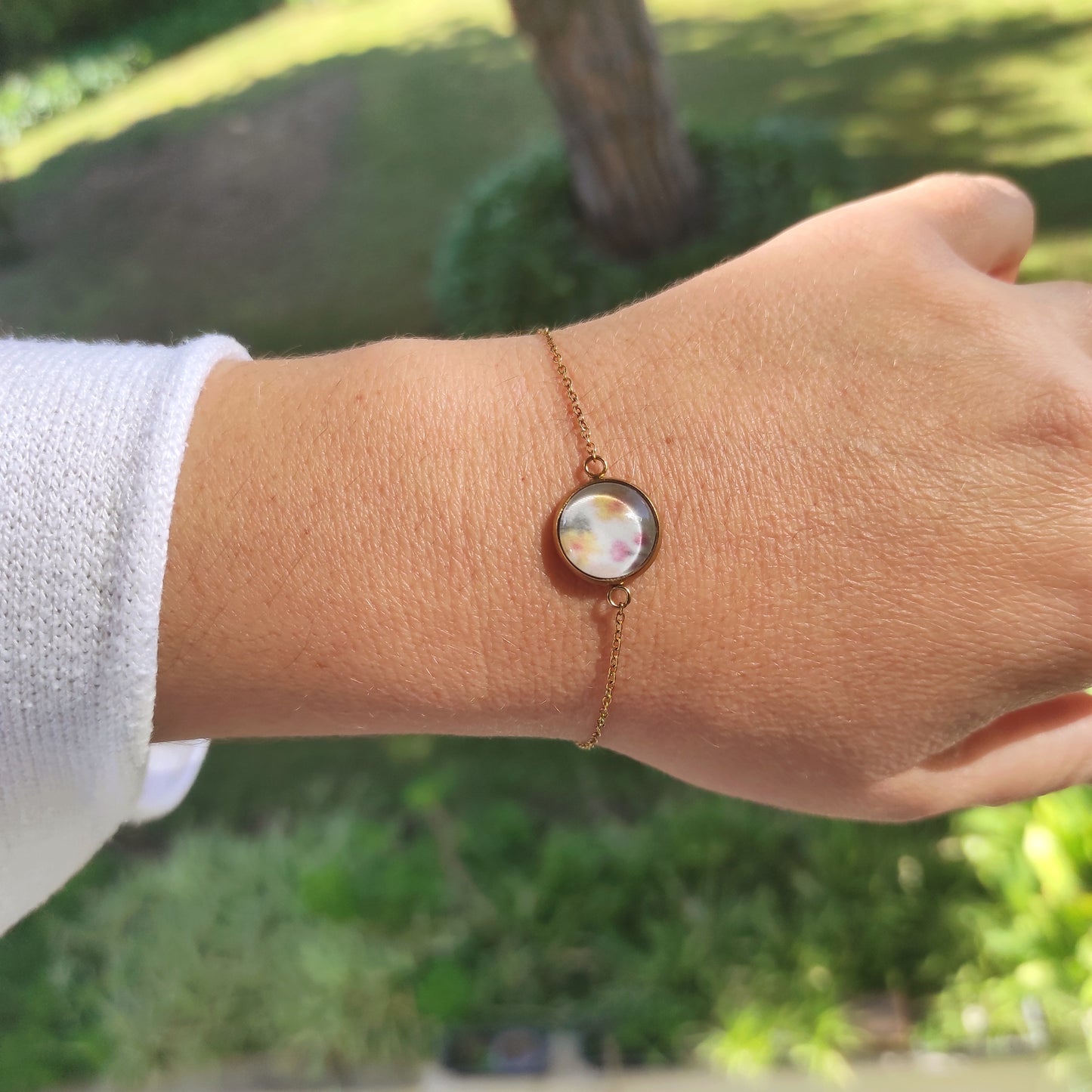 Bracelet réglable acier inoxydable couleur doré positionné sur un poignet. Le motif à l'intérieur comporte plusieurs fleurs, jaune, rose et feuilles vertes avec un fond blanc. Perle de 12 mm de diamètre.