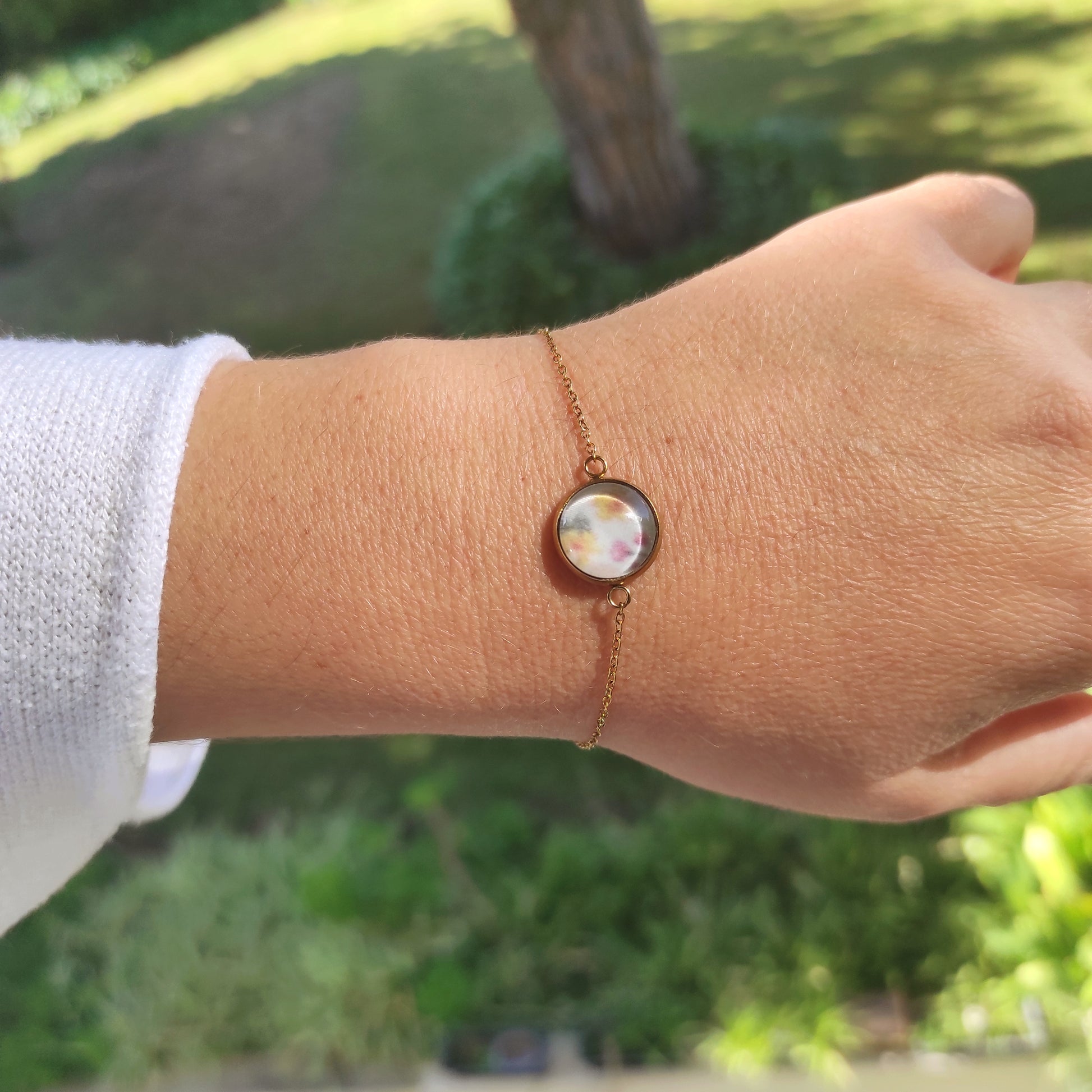 Bracelet réglable acier inoxydable couleur doré positionné sur un poignet. Le motif à l'intérieur comporte plusieurs fleurs, jaune, rose et feuilles vertes avec un fond blanc. Perle de 12 mm de diamètre.