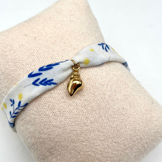 Bracelet en tissu signé Fanny Agustin, le motif est bleu jaune et blanc, il représente du mimosa. La breloque est un coquillage doré. 