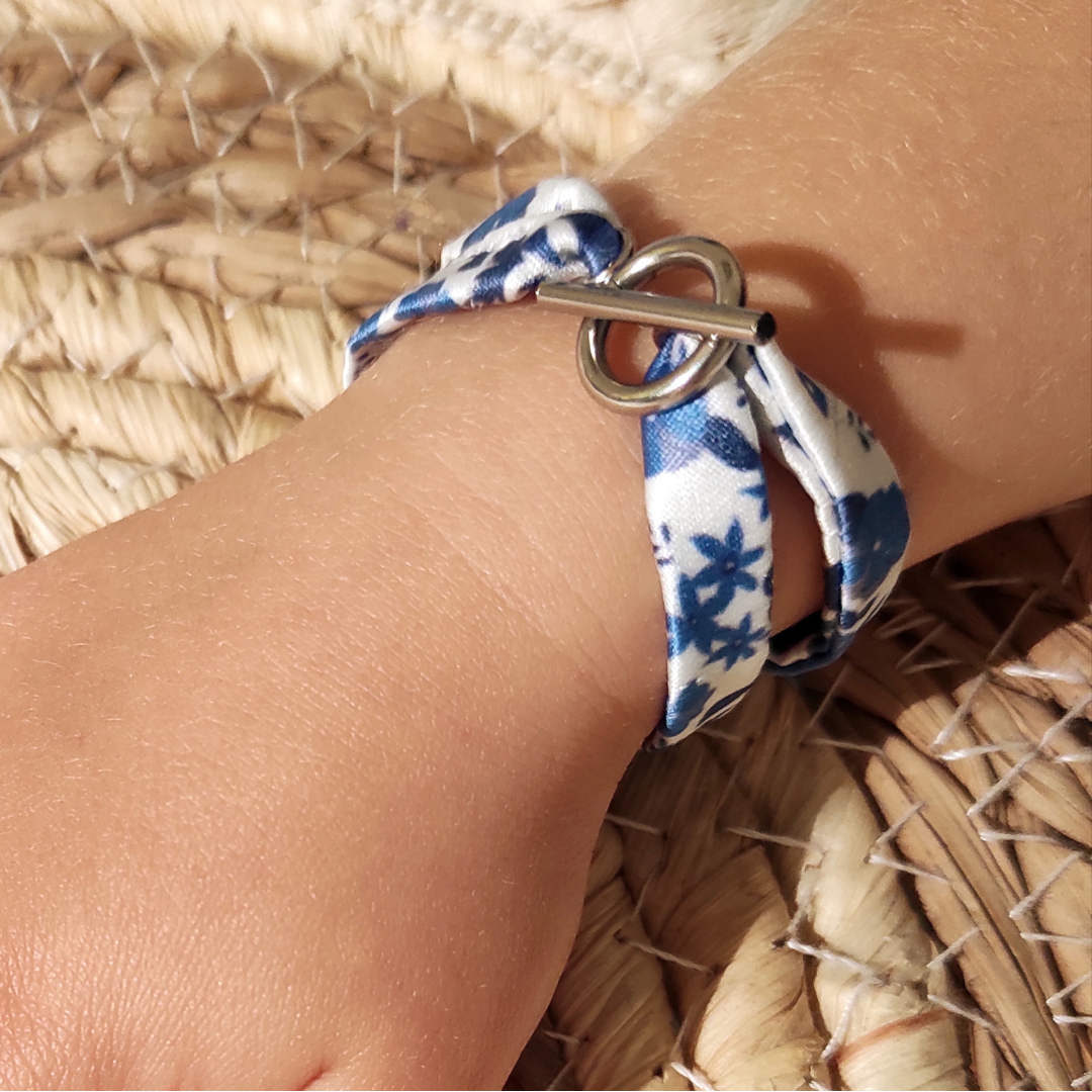 Bracelet en tissu satin motif fleurs bleues porté par petite fille, avec fermoir anneau en acier inoxydable.