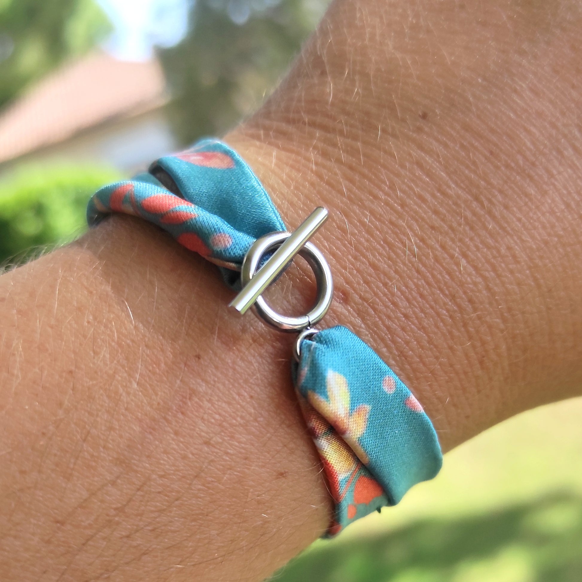 Bracelet en tissu satin motif vert et fleurs colorées orange et jaune avec fermoir anneau en acier inoxydable.