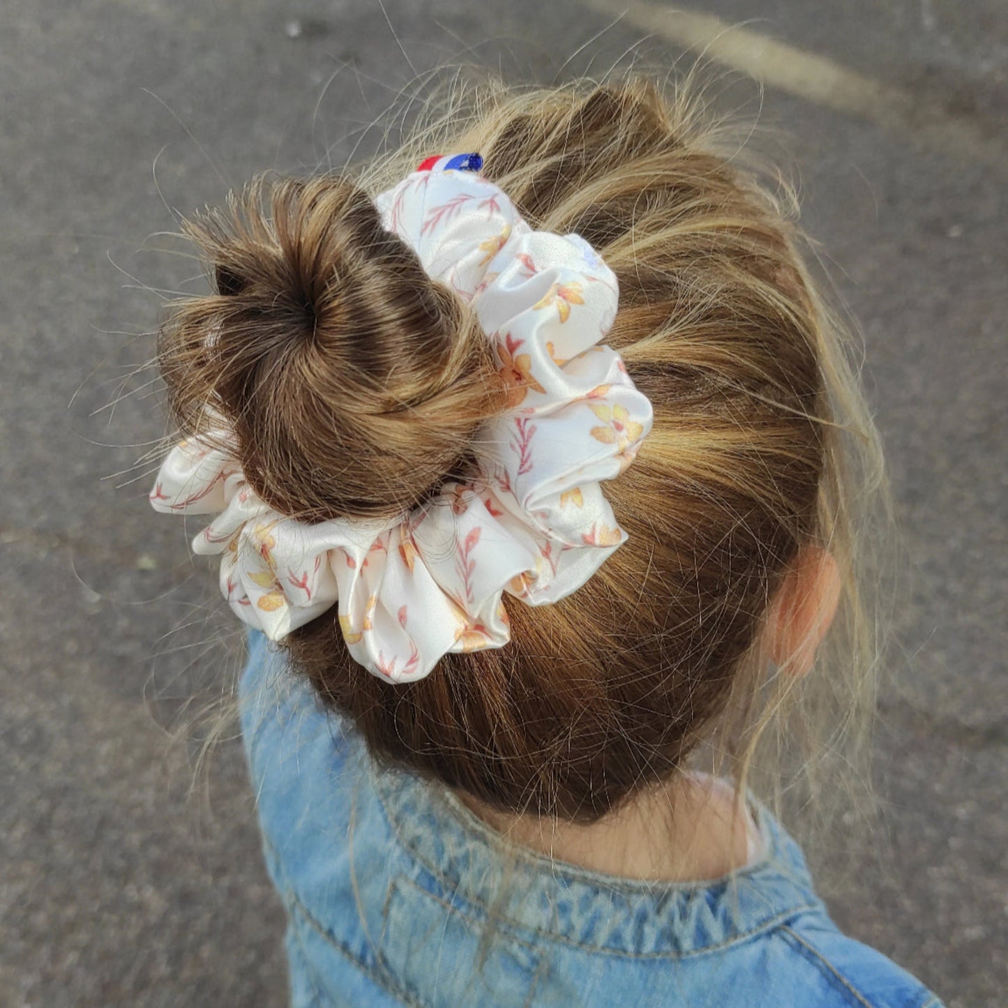 Chouchou fleurs dorées porté sur fillette. Gros chouchou en satin motif fleurs dorées, porté sur fillette avec chignon. Le fond du motif est blanc, les fleurs sont dorées avec quelques touches de feuillage marron. Création Fanny Agustin.