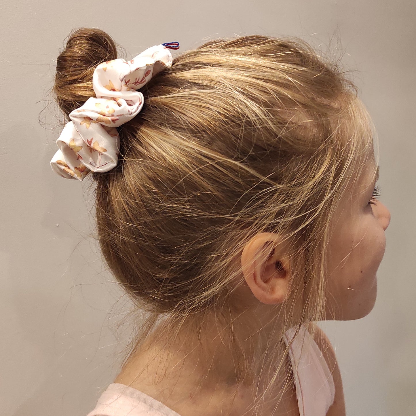 Chouchou satin porté sur fillette, avec tenue de danse classique. Le motif est fleurs dorées.