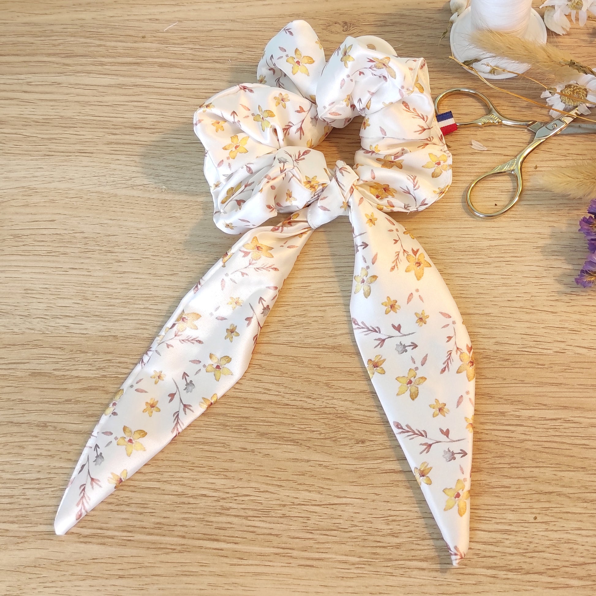 Chouchou foulchie motif fleurs dorées avec fond blanc. Le tissu en satin comporte également des feuilles marron et petites fleurs blanches.