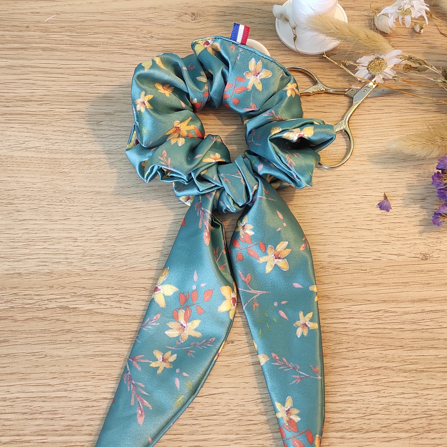 Chouchou foulchie avec motif fleuri, fleurs jaunes, feuilles orange et marron, fond vert. 