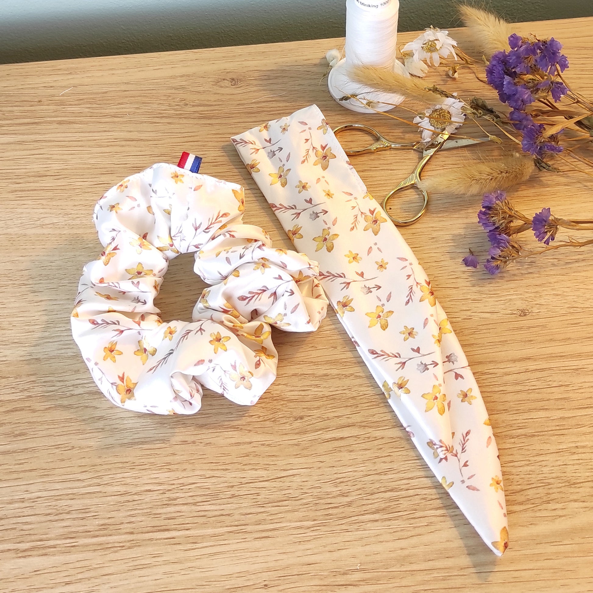 Chouchou foulchie motif fleurs dorées, avec du jaune, marron et fond blanc. La photo montre le ruban détaché à côté du chouchou.