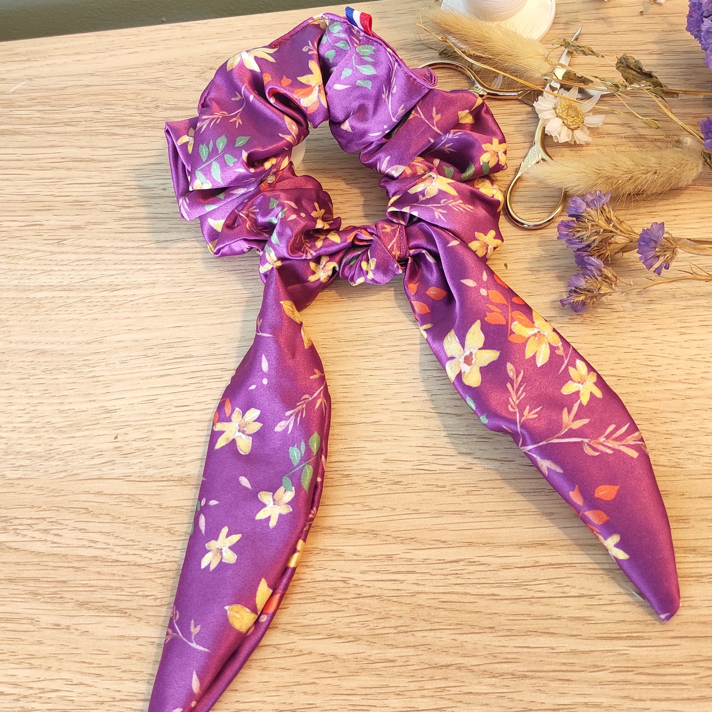 Chouchou foulchie motif fleuri avec fleurs jaunes, feuillage marron, orange et vert sur fond violet.