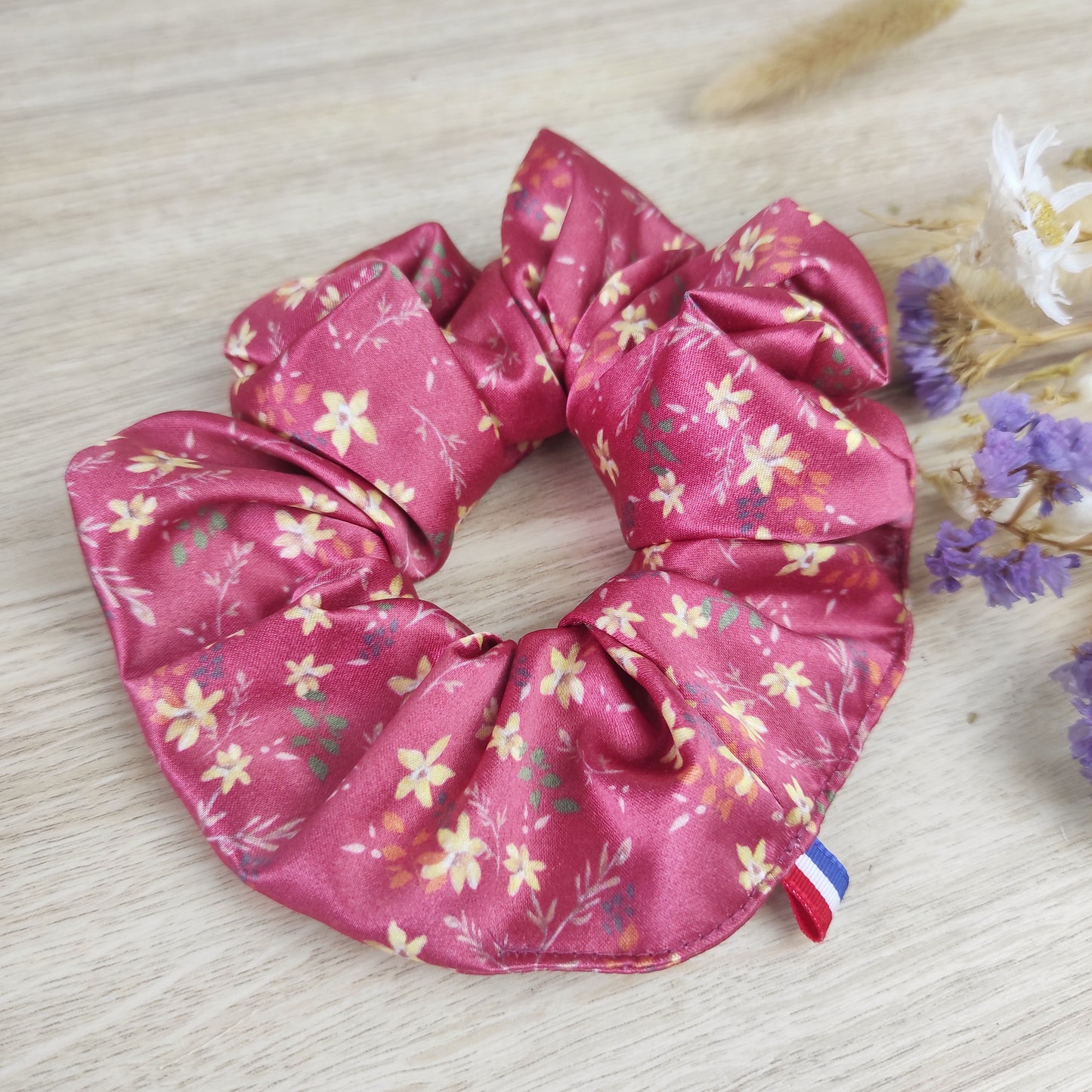 Accessoire cheveux en satin fleuri rouge, motif dessiné par Fanny Agustin. Le chouchou comporte de petites fleurs jaunes, feuille oranges et vertes, le fond est rouge.