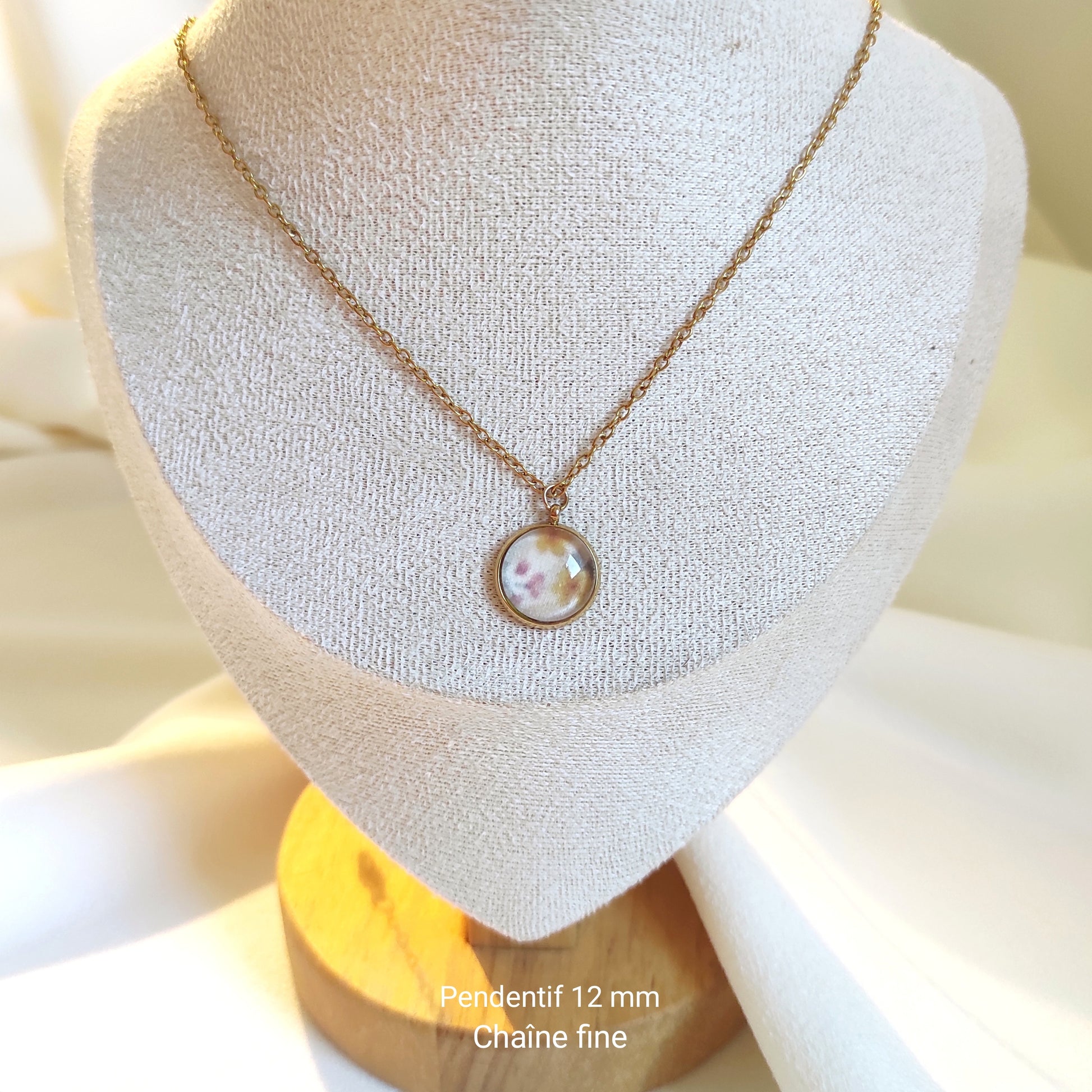 Collier doré avec perle de 12 mm et chaîne fine sur présentoir. Le motif est de petites fleurs dessinées en aquarelle et imprimé sur tissu. Il y a du jaune, rose, vert et fond blanc, motif délicat et discret. Détail de la photo avec les tailles.