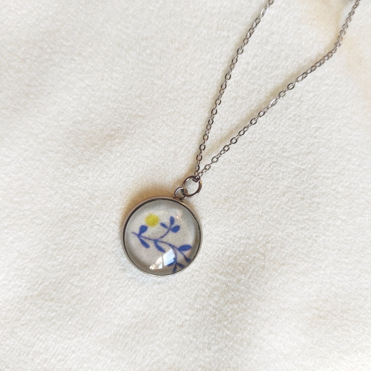 Collier acier inoxydable fait main, détail du motif sous la perle, feuilles bleues et point jaune.