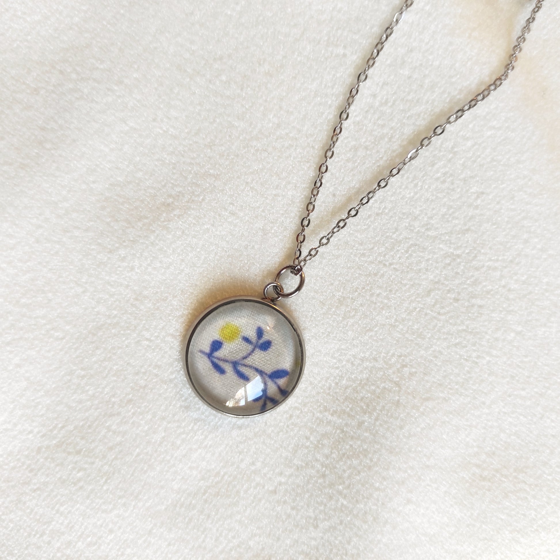 Collier acier inoxydable fait main, détail du motif sous la perle, feuilles bleues et point jaune.