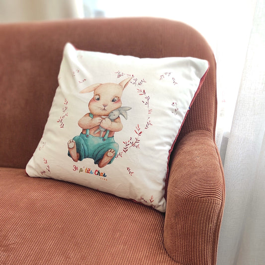 Coussin motif lapin avec fond blanc en velours placé sur un canapé.