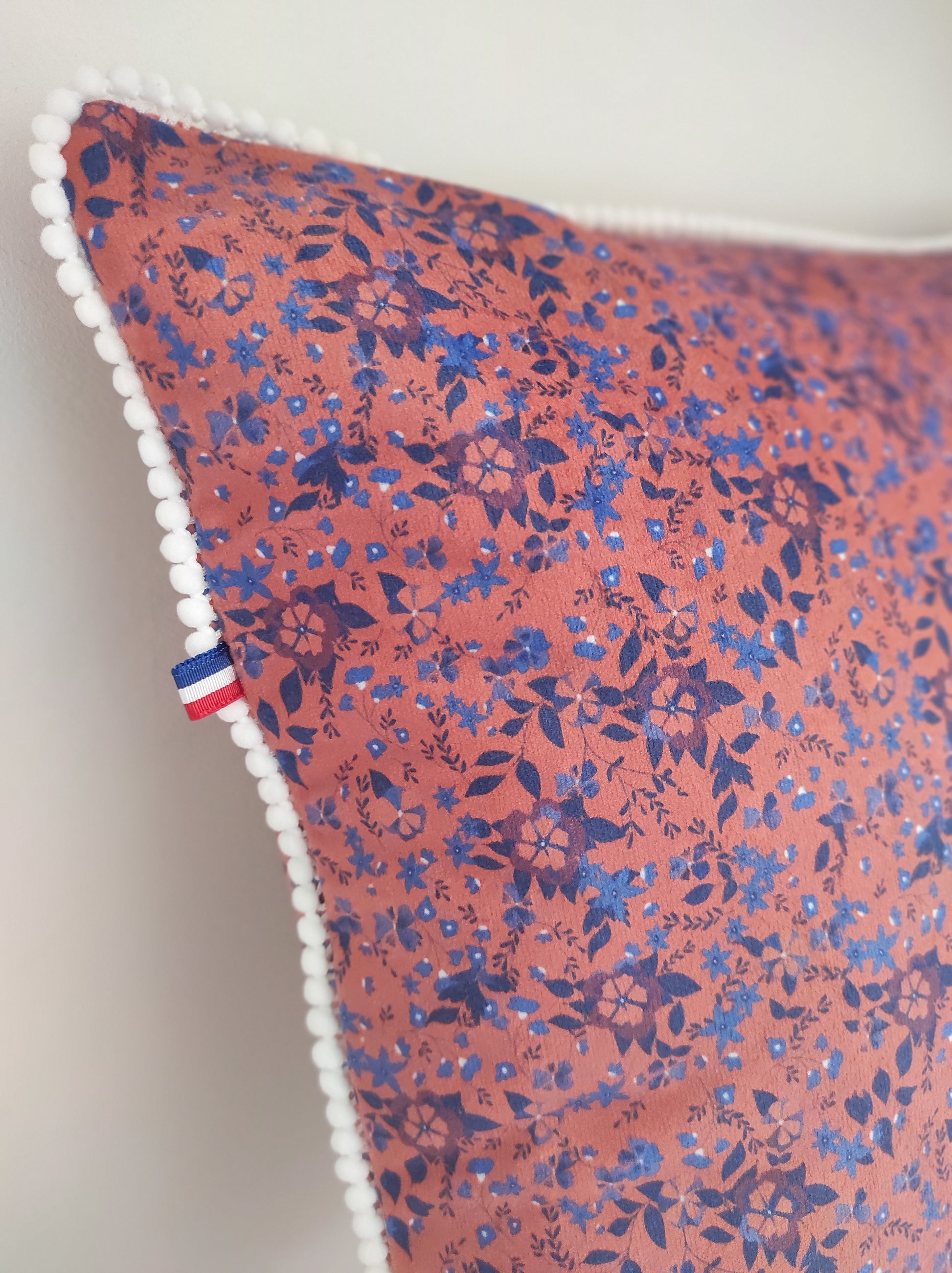 Coussin velours fleuri paprika avec détail ruban pompons.