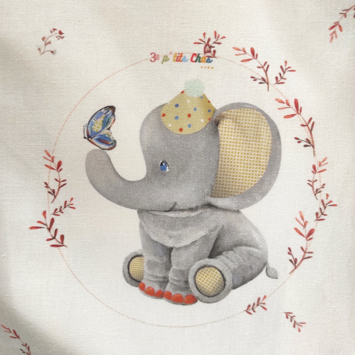 Eléphant dessiné à l'acrylique puis imprimé sur tissu en coton. Dessin exclusifs de FANNY AGUSTIN. L'éléphant est assis avec un papillon sur le nez. Il  un chapeau de clown sur la tête. Ses oreilles sont jaunes et le dessous de ces pattes également. Il est entouré de feuillage marron sur fond blanc.