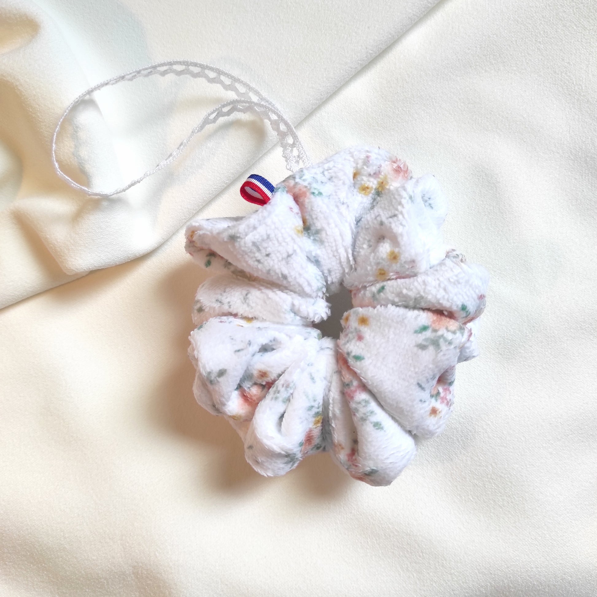 Fleurs de douche motif fleurs aquarelle dessiné par Fanny Agustin. Les fleurs sont orange, roses, jaunes avec quelques touches de feuilles vertes sur fond blanc. Un ruban en dentelle pour accrocher au poignet est présent avec ruban bleu blanc rouge, made in France.