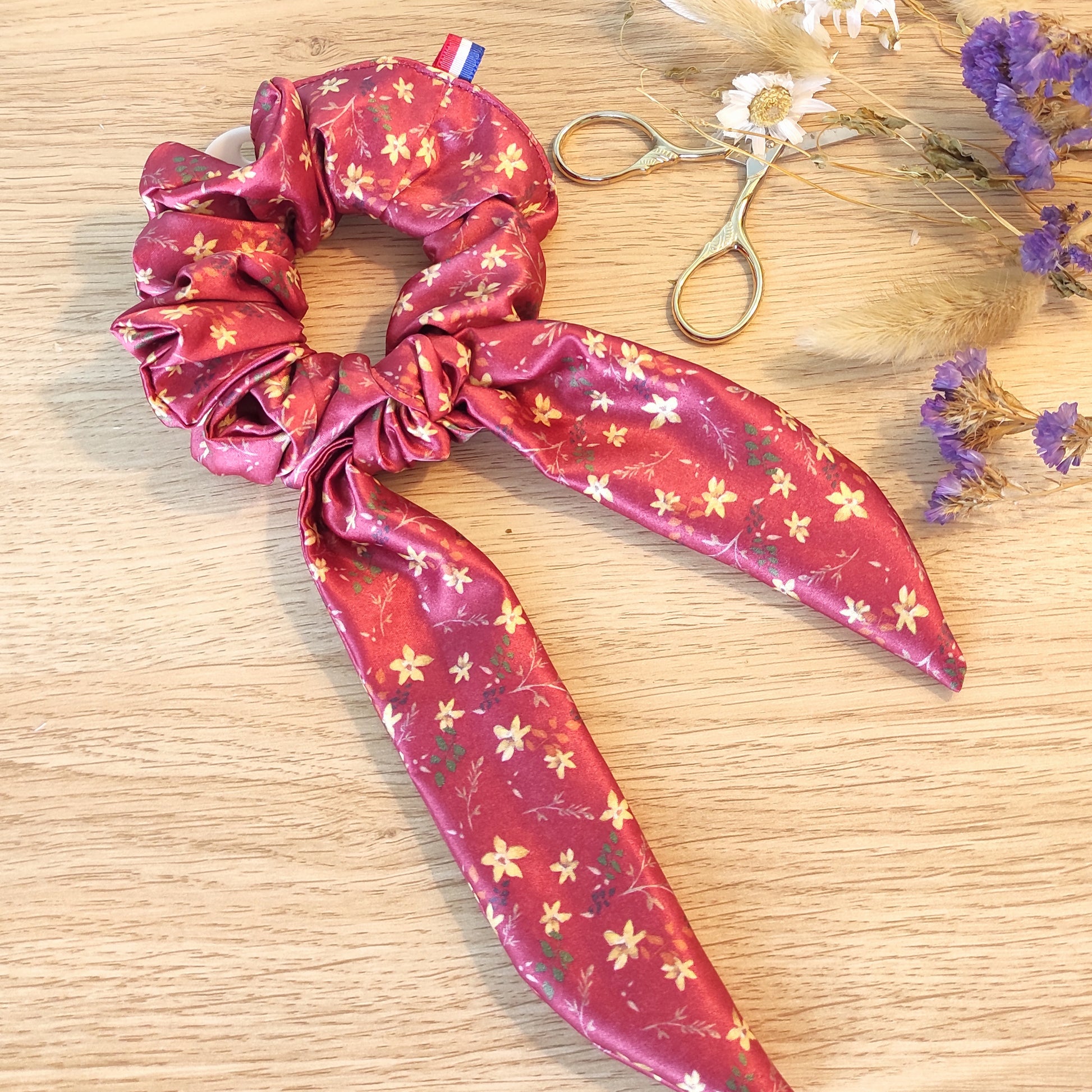 Chouchou foulchie motif fleuri, petites fleurs jaunes et feuillage marron, orange et vert, sur fond rouge.