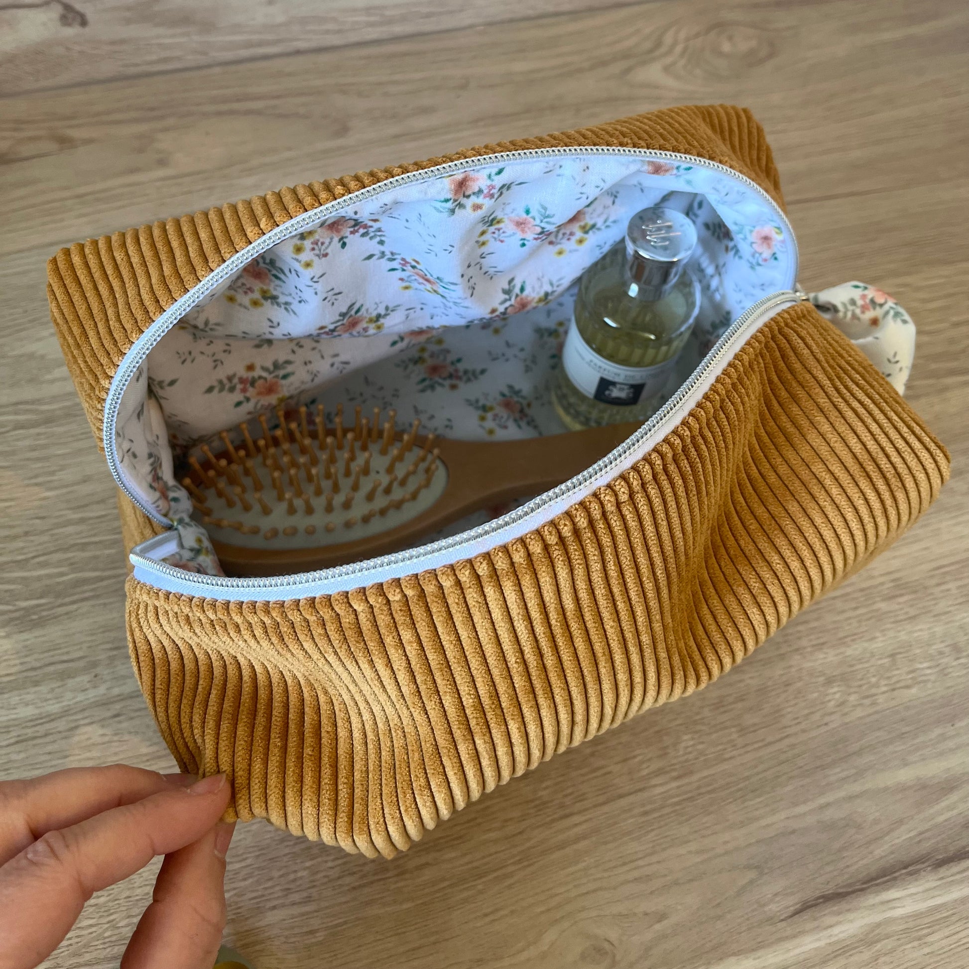 Grosse trousse de toilette en velours côtelé de couleur jaune moutarde, avec fermeture éclair argentée, logo et ruban bleu blanc rouge, fabrication Française artisanale. Sur la photographie, la trousse est ouverte et laisse entrevoir une brosse à cheveux et parfum.