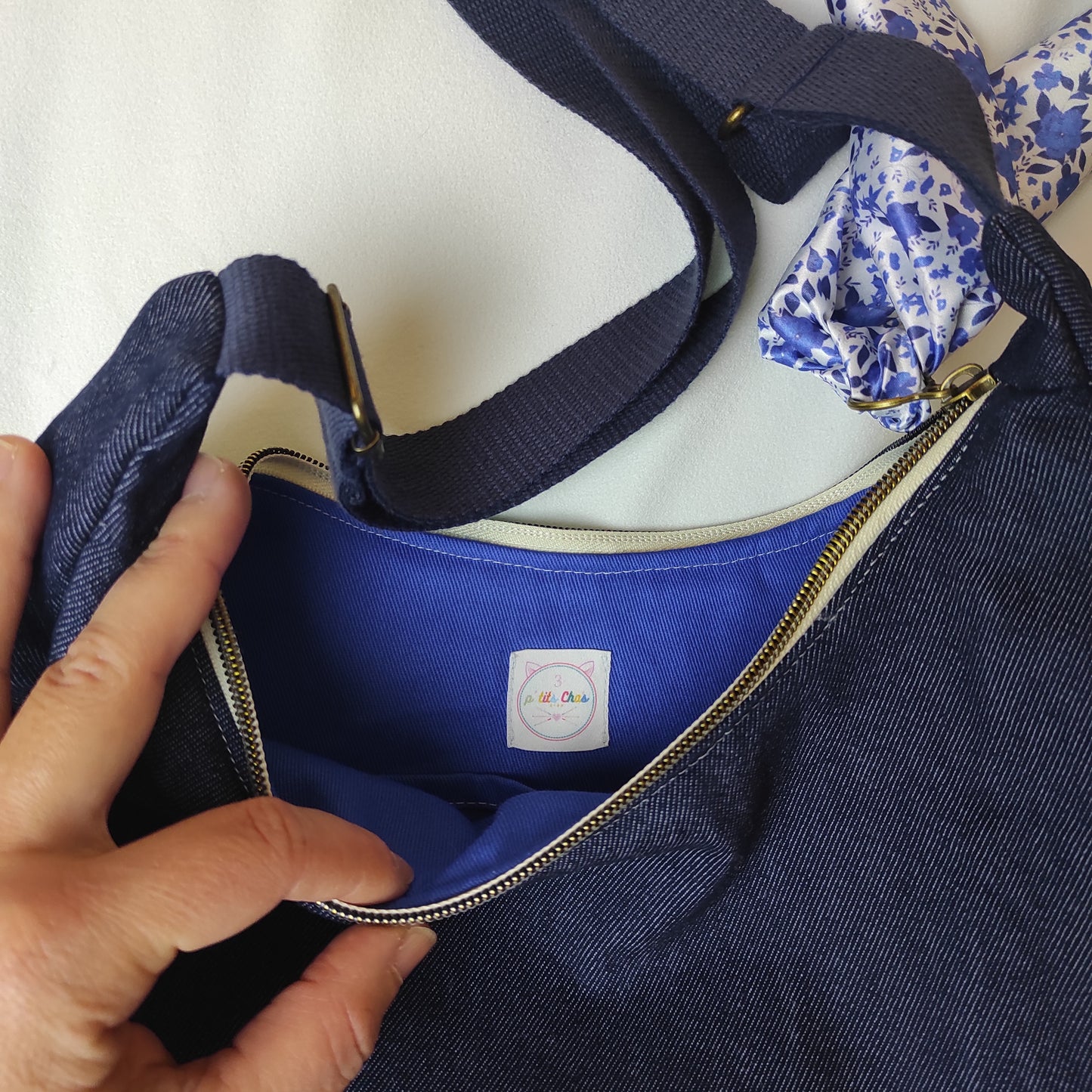 Une main ouvre le sac et laisse apparaître la doublure bleu klein, assorti au ruban, avec le logo.