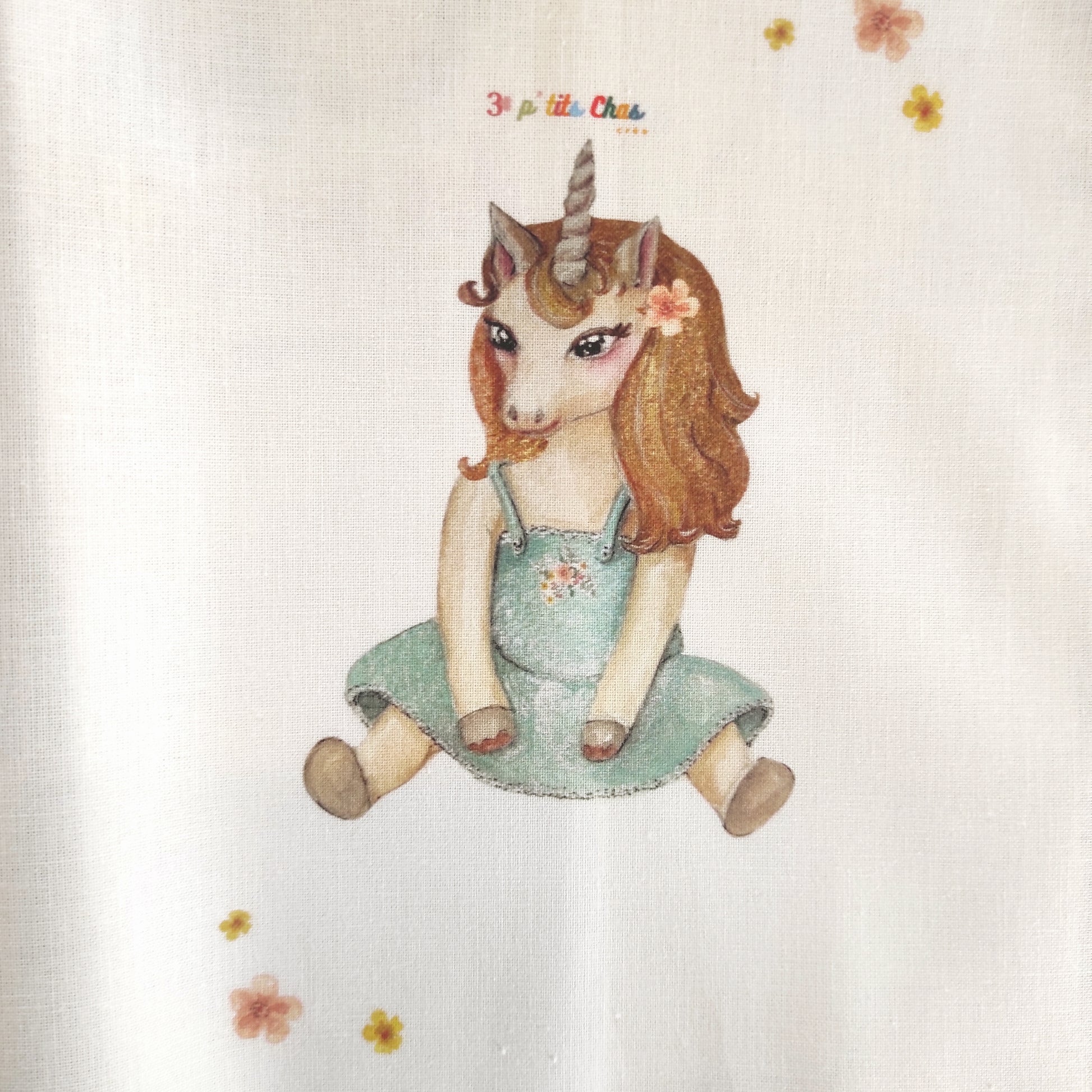 Licorne dessinée à l'aquarelle puis imprimée sur tissu en coton. Dessin exclusifs de FANNY AGUSTIN. La licorne est assise avec une robe bleue et une fleur orange dans les cheveux.