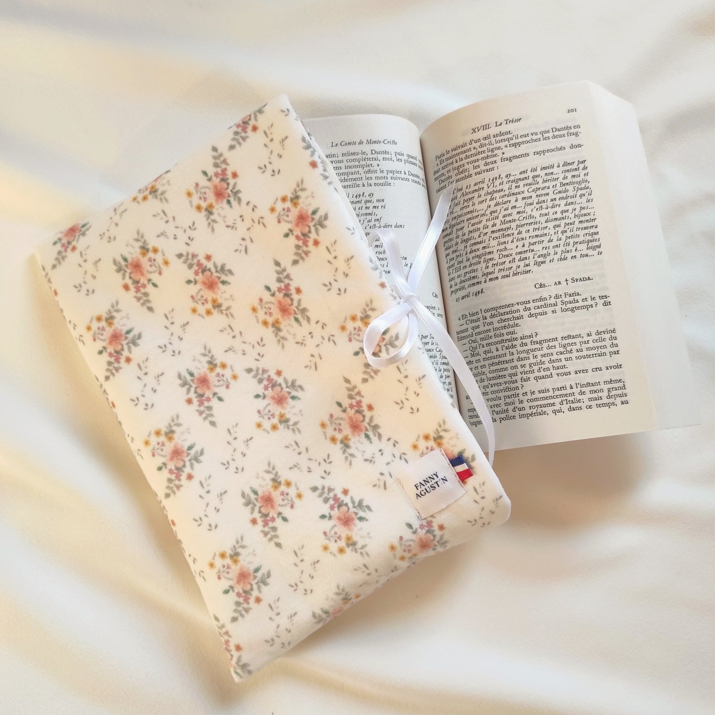 Pochette à livre en velours fleuri avec fleurs oranges, jaunes et roses et quelques feuilles vertes sur fond blanc. Le motif est dessiné par Fanny Agustin, puis fabriqué artisanalement à Cagnes-sur-Mer en France.