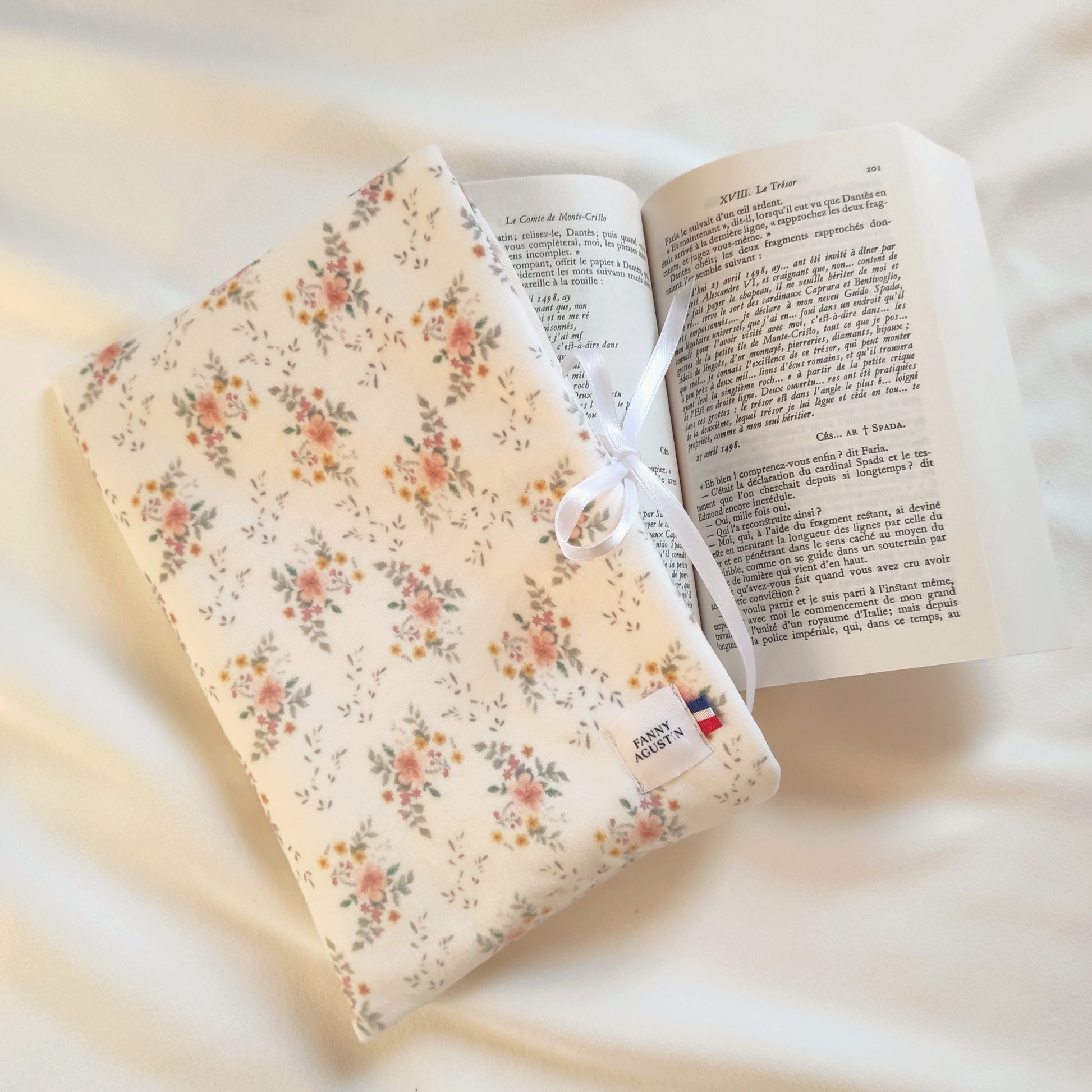 Pochette à livre en velours fleuri avec fleurs oranges, jaunes et roses et quelques feuilles vertes sur fond blanc. Le motif est dessiné par Fanny Agustin, puis fabriqué artisanalement à Cagnes-sur-Mer en France.