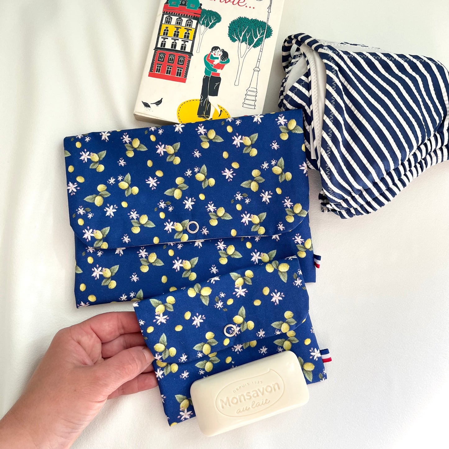 Pochette de taille standard pour protéger un livre de poche dans un sac de plage ou placer son maillot de bain mouillé. Dessin et fabrication de Fanny Agustin. Sur la photographie se trouve deux pochettes de taille différente, avec motif citron fond bleu.