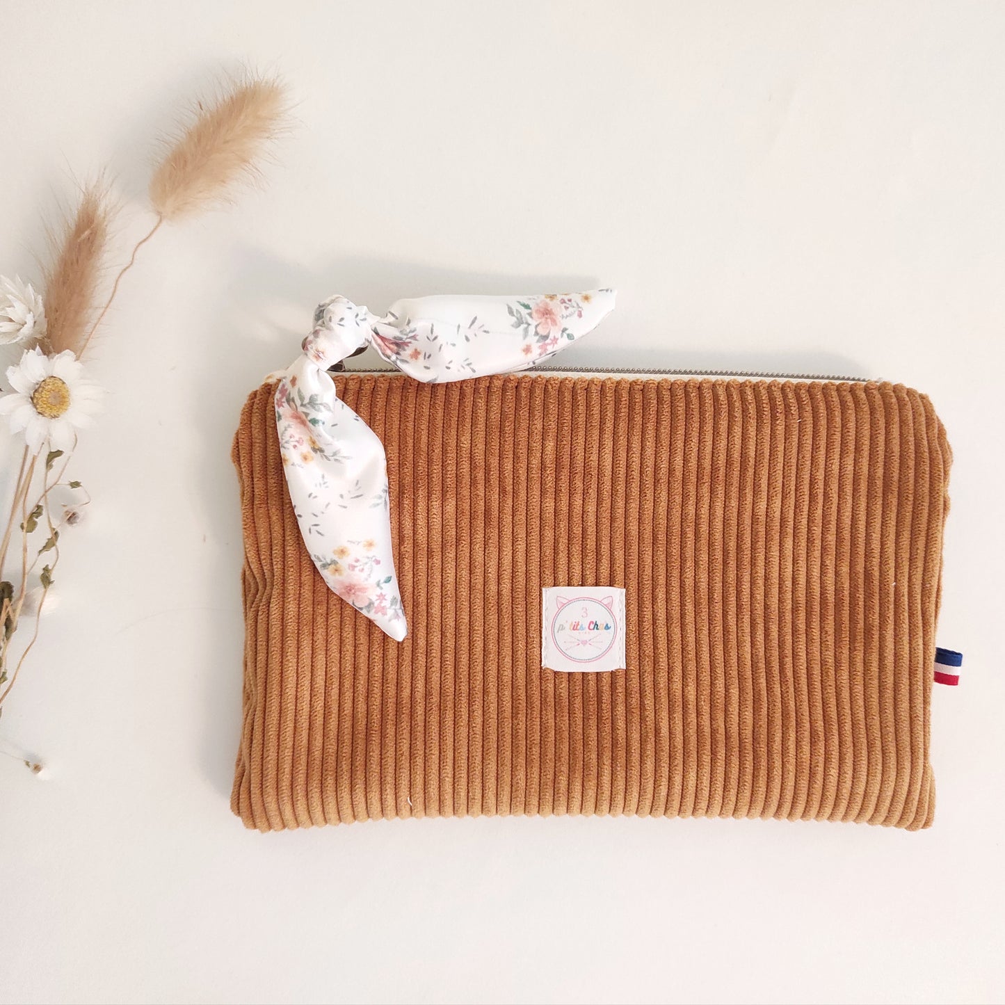Pochette en velours jaune avec ruban fleuri et logo blanc placé au centre.