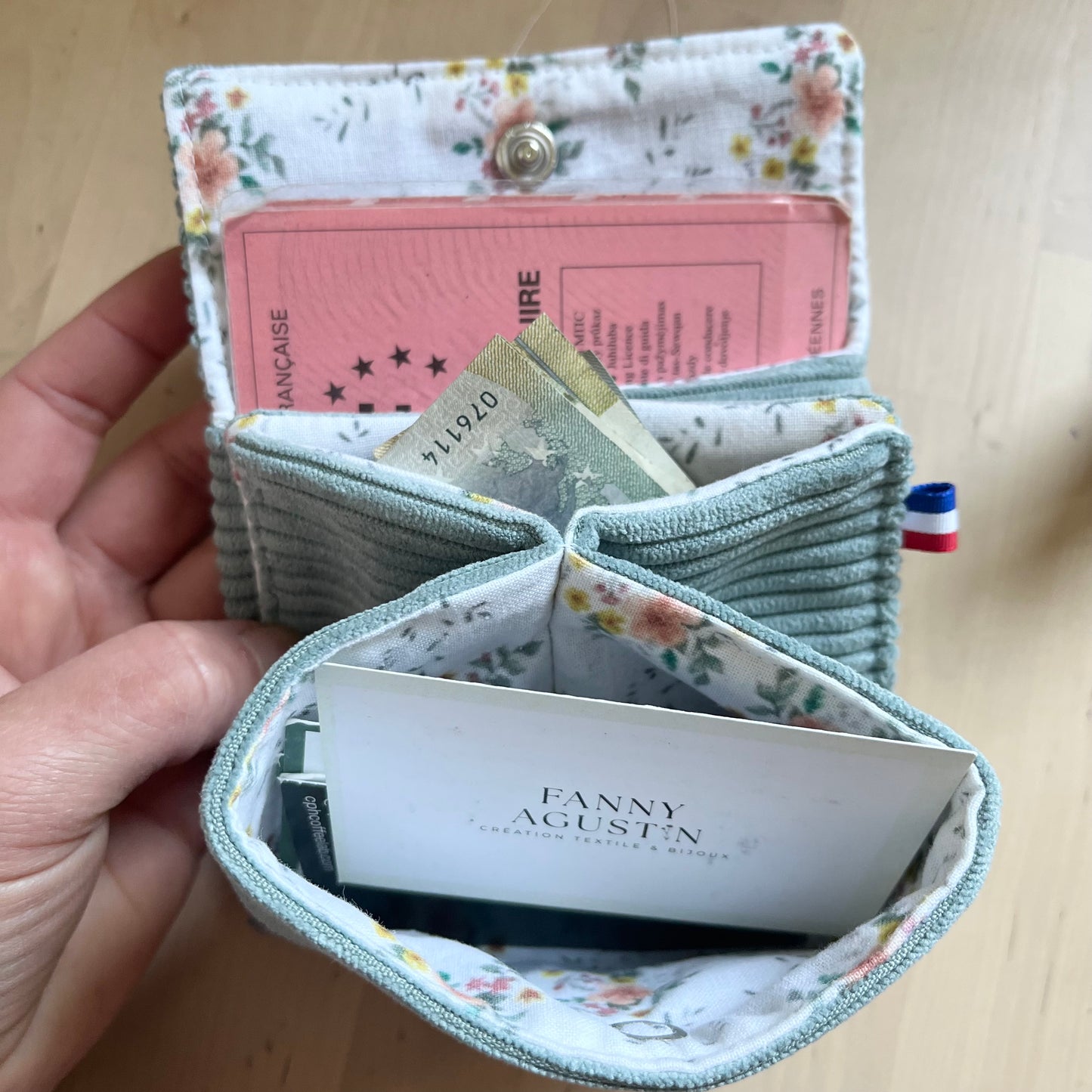 Porte-monnaie multifonction, en velours côtelé avec doublure fleurie dessinée par Fanny Agustin. Sur la photographie, un porte monnaie est ouvert, on peut y insérer un permis de conduire, des cartes et billets.