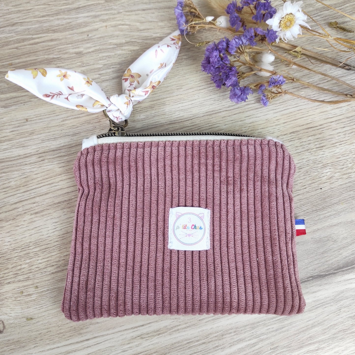 Porte monnaie avec ruban fleuri et velours rose, petit ruban made in France sur le côté et logo blanc placé au centre du porte monnaie.