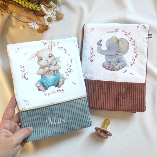 Protèges carnets de santé personnalisés, avec choix du velours côtelé et dessin, option broderie. Sur la photo, on trouve 2 protèges carnets avec motif lapin et velours vert de gris, ruban doré et prénom brodé en blanc sur le velours. Le second protège carnet est marron avec motif éléphant.