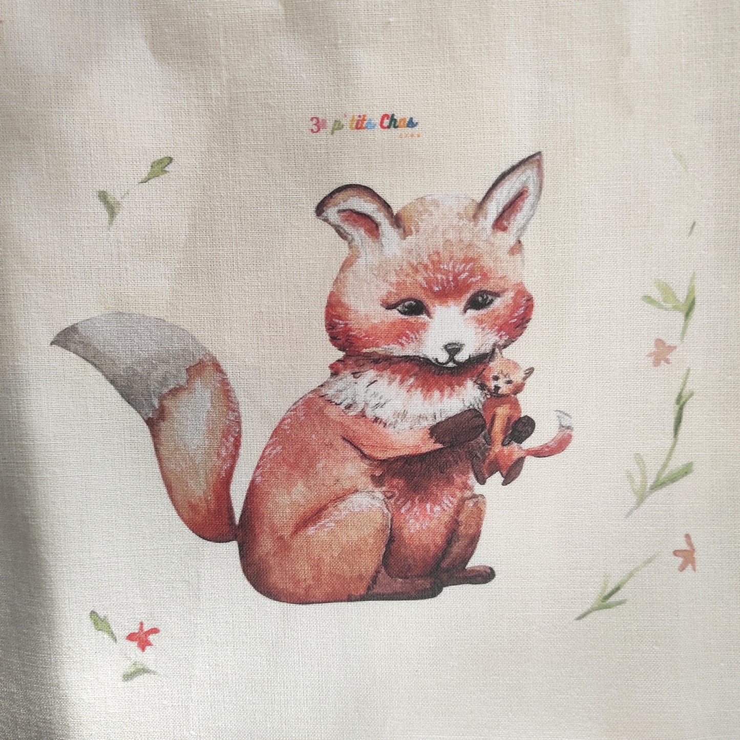 Renard dessiné à l'aquarelle puis imprimé sur tissu en coton. Dessin exclusifs de FANNY AGUSTIN. Le renard tient un doudou dans ses bras et est entouré de feuillage et fleurs oranges.