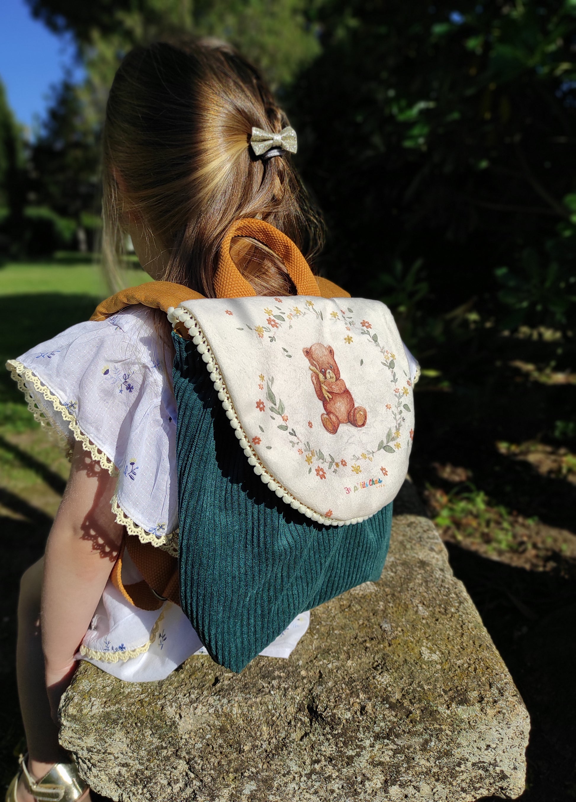 Sac à dos porté sur fillette, motif ourson fond écru avec dentelle écrue en pompons et velours côtelé vert de gris.