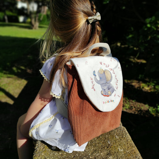 Sac à dos porté sur fillette, avec motif éléphant et velours côtelé marron.